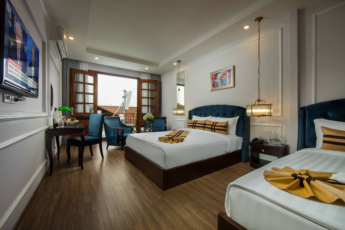 A hotel room with two beds, a desk with a chair, a TV, and a large window.