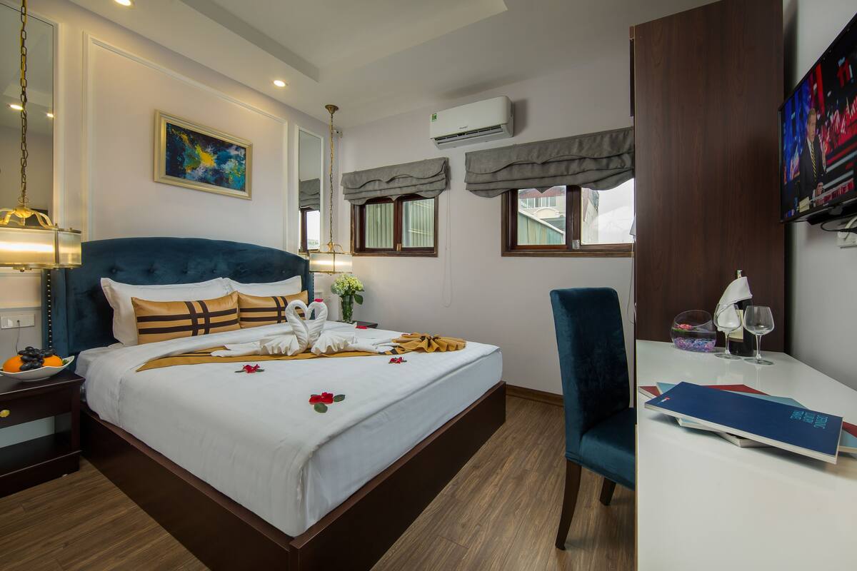 A hotel room with a large bed, a desk with a chair, a TV, and an air conditioning unit.