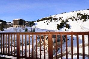 A snow-covered ski resort with buildings, a parking lot, and a mountain backdrop.