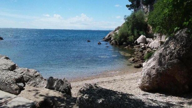 Eine felsige Küstenlinie mit klarem, blauem Wasser, einem Sandstrand und etwas Grün.