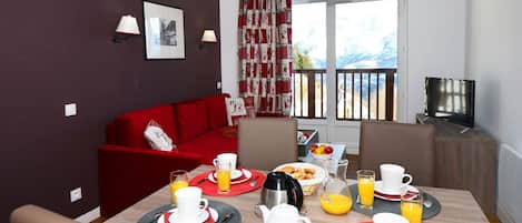 A dining area with a red sofa, a TV, and breakfast items on the table.