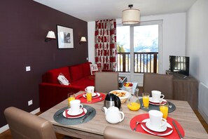 A dining area with a red sofa, a TV, and breakfast items on the table. - Retreat Steps from Ski Lifts (Auris)
