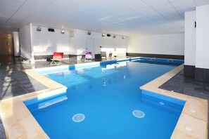An indoor swimming pool with multiple lanes, a tiled floor, and several lounge chairs.