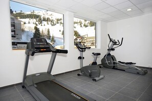 A gym with treadmills, an elliptical, and a stationary bike, featuring large windows with a snowy mountain view.