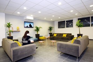 A modern waiting area with grey sofas, a television, and potted plants.