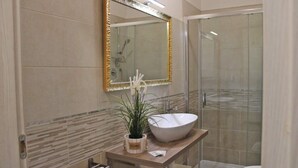 A modern bathroom with a large mirror, a white sink, and a glass shower enclosure. - 03. Apartment (Signa)