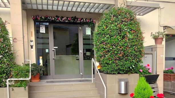 A hotel entrance with a glass door, steps leading up to it, and potted plants around. - 03. Apartment (Signa)