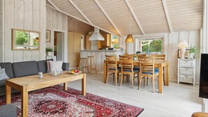 A cozy, open-plan living and dining area with a wooden ceiling, a dining table with chairs, a sofa, and a red patterned rug. - Amazing home in Sjællands Odde (Sjællands Odde)