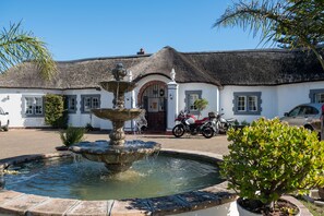 A building with a thatched roof, a fountain, and a potted plant.