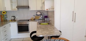 A compact kitchen with white cabinets, a stainless steel stove, a sink, and a toaster. - The Sanctuary Guest House Estate (Cape Town)