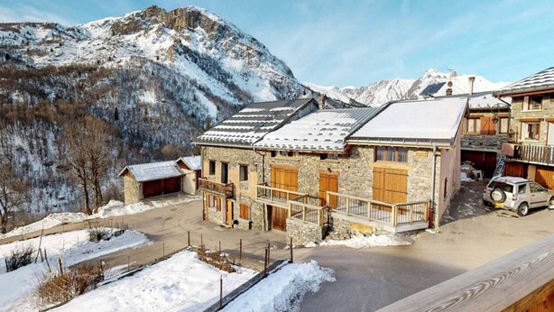 A stone building with a snow-covered roof, a car parked in front, and a mountain in the background.