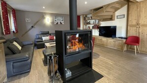 A living room with a black wood-burning stove, a grey sofa, a red chair, a television, and wooden cabinets.