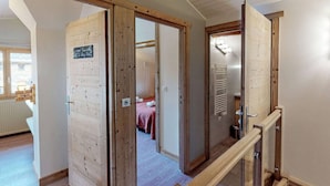 A wooden interior with a staircase, a visible bathroom, and a bed in the adjacent room.