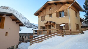 A multi-story chalet with a wooden exterior, a balcony, and a snow-covered landscape.