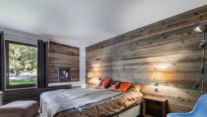 A modern bedroom with a large bed, two bedside lamps, a blue chair, and a view of greenery outside. - Duplex 2-bed apartment, terrace, near slopes in Megève (Megève)