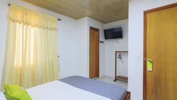 Quarto com uma cama, televisão fixada na parede e porta de madeira.