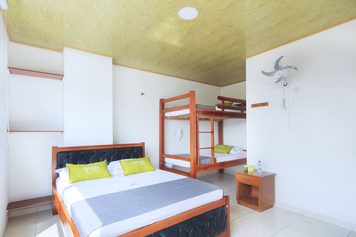 Une chambre comprenant un lit, un lit superposé, une table de chevet et un ventilateur fixé au mur.