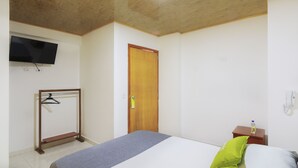 Ein Schlafzimmer mit einem Bett, einer Holztür, einem an der Wand montierten Fernseher und einem kleinen Tisch mit einer Flasche.