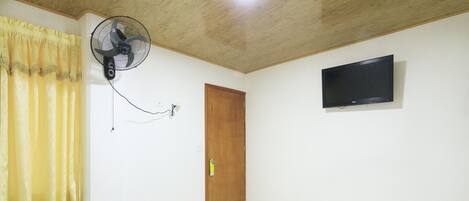 Un dormitorio con cama, televisión montada en la pared, ventilador de techo y puerta de madera.