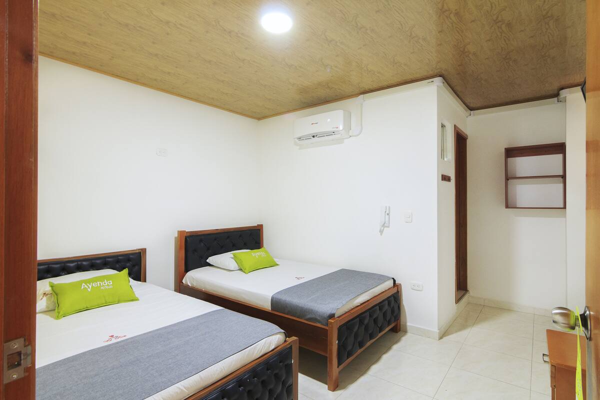 Une chambre avec deux lits, chacun recouvert d’une couverture grise et doté d’un oreiller, et une tête de lit en bois.