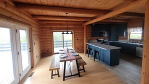 A wooden cabin interior with a dining area, kitchen, and large windows. - Nolin Lake Log Cabin ~ Beautiful Water Views ~ Great Family Getaway!  (Mammoth Cave)
