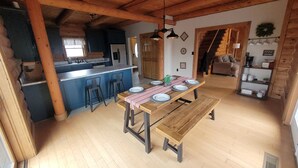 A spacious kitchen with a central island, wooden dining table with benches, and a cozy living area with a sofa and coffee table. - Nolin Lake Log Cabin ~ Beautiful Water Views ~ Great Family Getaway!  (Mammoth Cave)