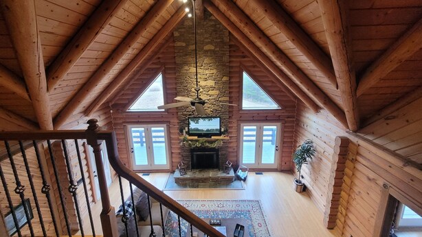 A spacious loft with a high ceiling, wooden beams, a stone fireplace, and a large TV. - Nolin Lake Log Cabin ~ Beautiful Water Views ~ Great Family Getaway!  (Mammoth Cave)