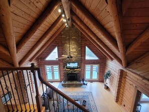 A spacious loft with a high ceiling, wooden beams, a stone fireplace, and a large TV.