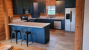A modern kitchen with granite countertops, a central island with bar stools, built-in appliances, and wooden beams. - Nolin Lake Log Cabin ~ Beautiful Water Views ~ Great Family Getaway!  (Mammoth Cave)