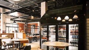 Un espace bar moderne avec des tables rondes, des fauteuils en cuir noir et un présentoir réfrigéré contenant des bouteilles.