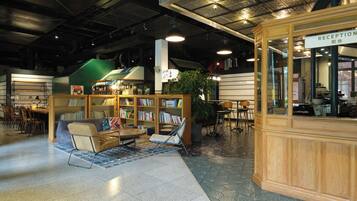 A reception area with a wooden reception desk, a seating area with a sofa and chairs, and a bookshelf filled with books.