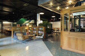 Un área de recepción con un mostrador de madera, una zona de estar con un sofá y sillones, y una estantería llena de libros.