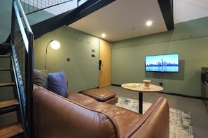 Een moderne woonkamer met een leren bank, een kleine ronde tafel en een televisie waarop een stadsgezicht te zien is.