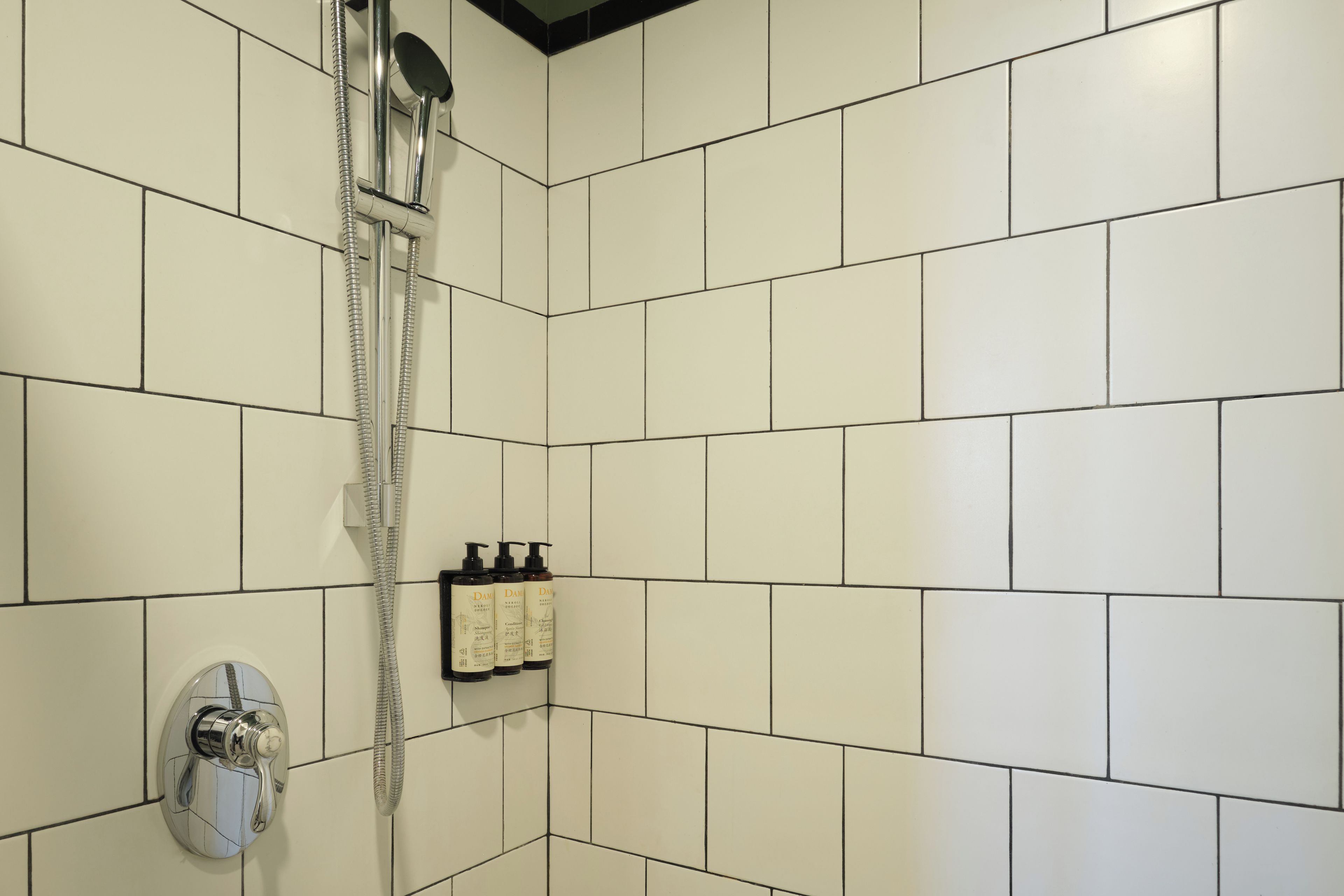 A bathroom with white tiled walls, a shower with a handheld showerhead, and a wall-mounted soap dispenser.