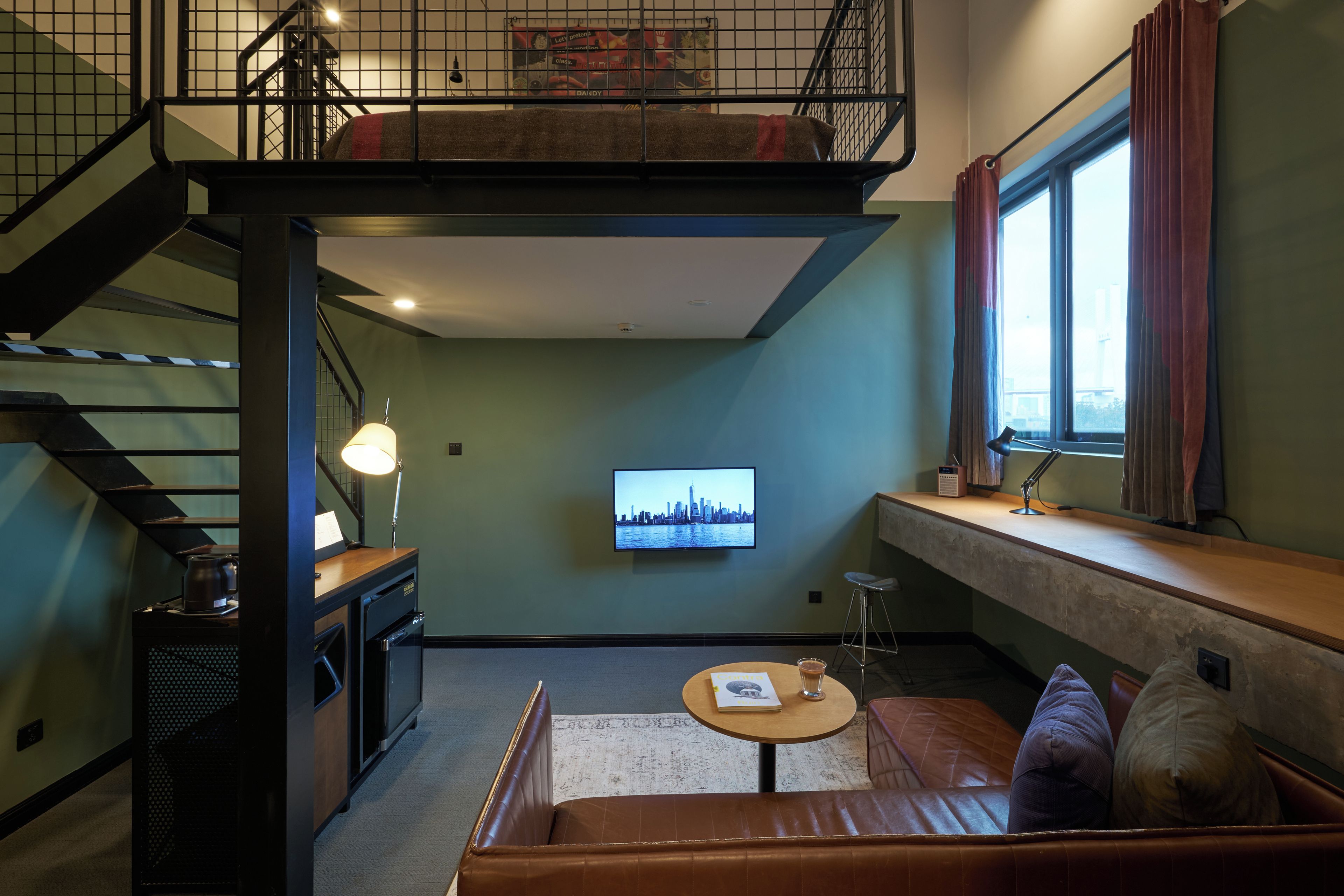 A loft-style room with a staircase, a television, a sofa, and a window with curtains.