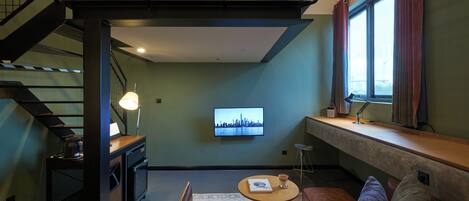 A loft-style room with a staircase, a television, a sofa, and a window with curtains.
