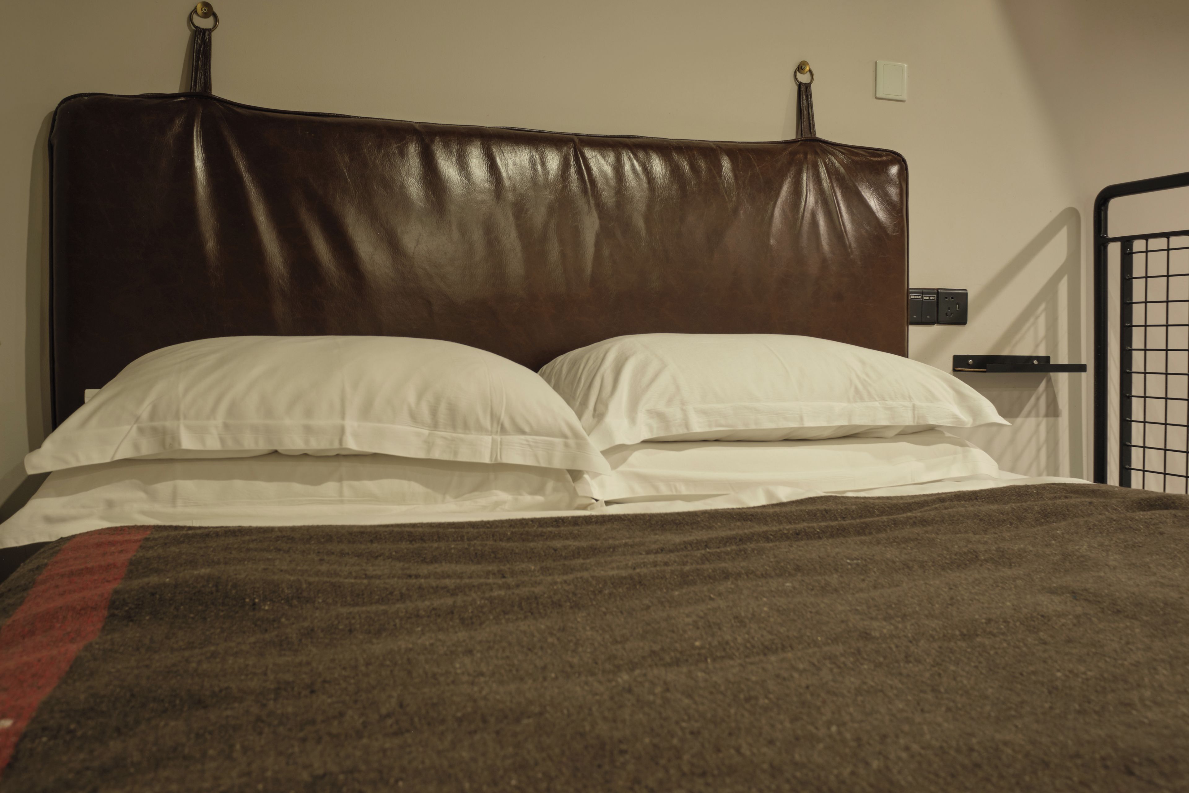 A bed with a brown headboard, white pillows, and a brown blanket.