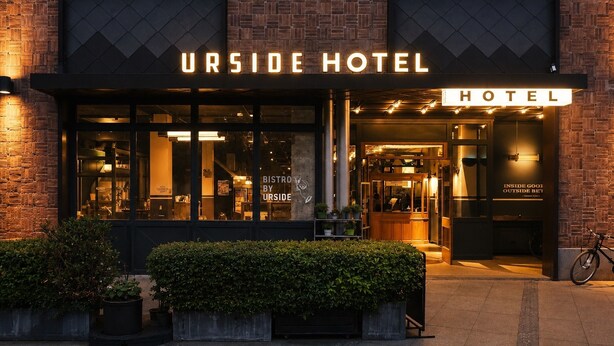L’extérieur de l’hôtel Urside se caractérise par sa façade en briques, ses grandes fenêtres et une enseigne indiquant la présence d’un bistrot.
