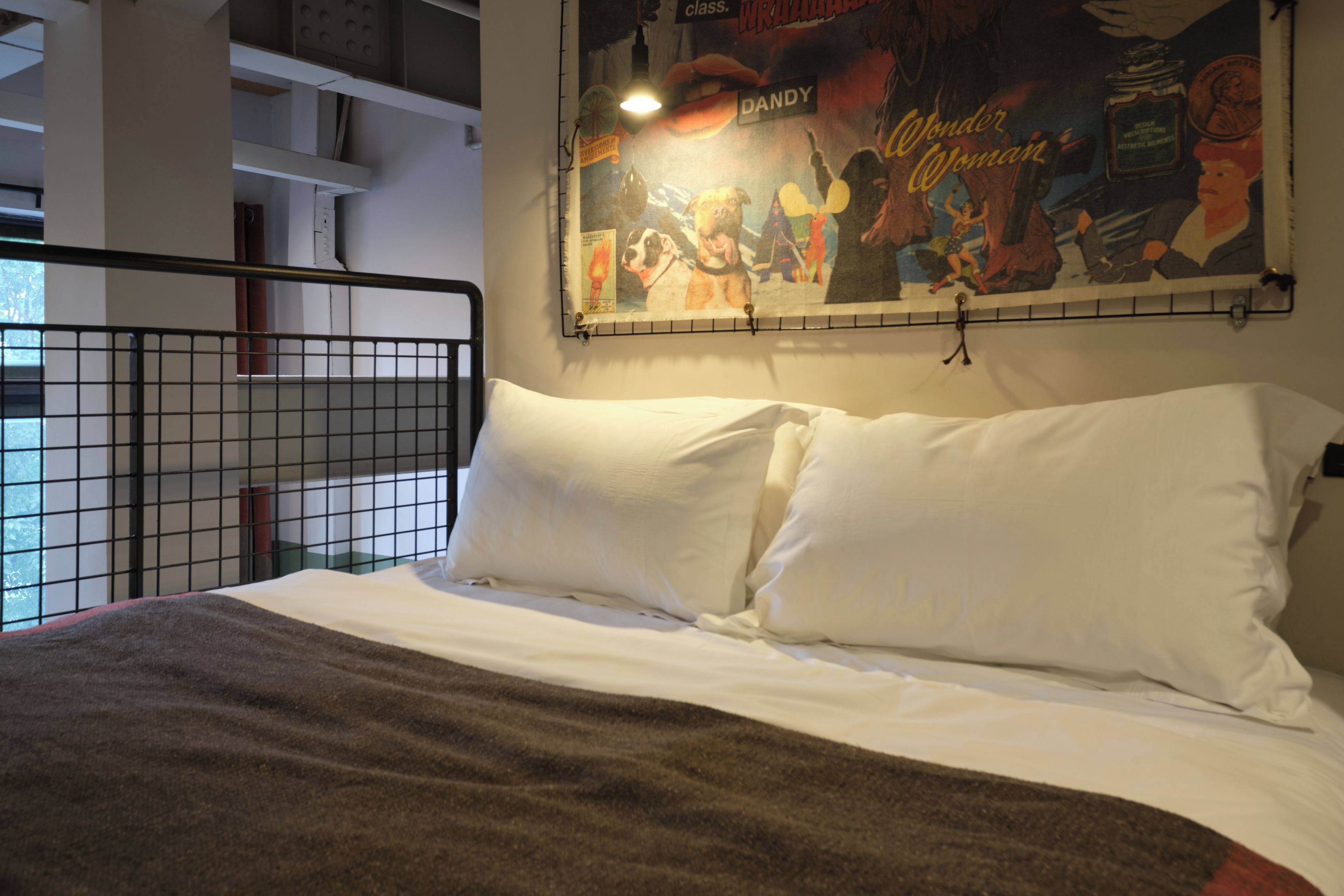 Una cama con ropa de cama blanca y una manta marrón, un pasamanos de metal y una pared con un póster.