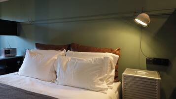 A neatly made bed with white linens, a brown headboard, and a bedside lamp.