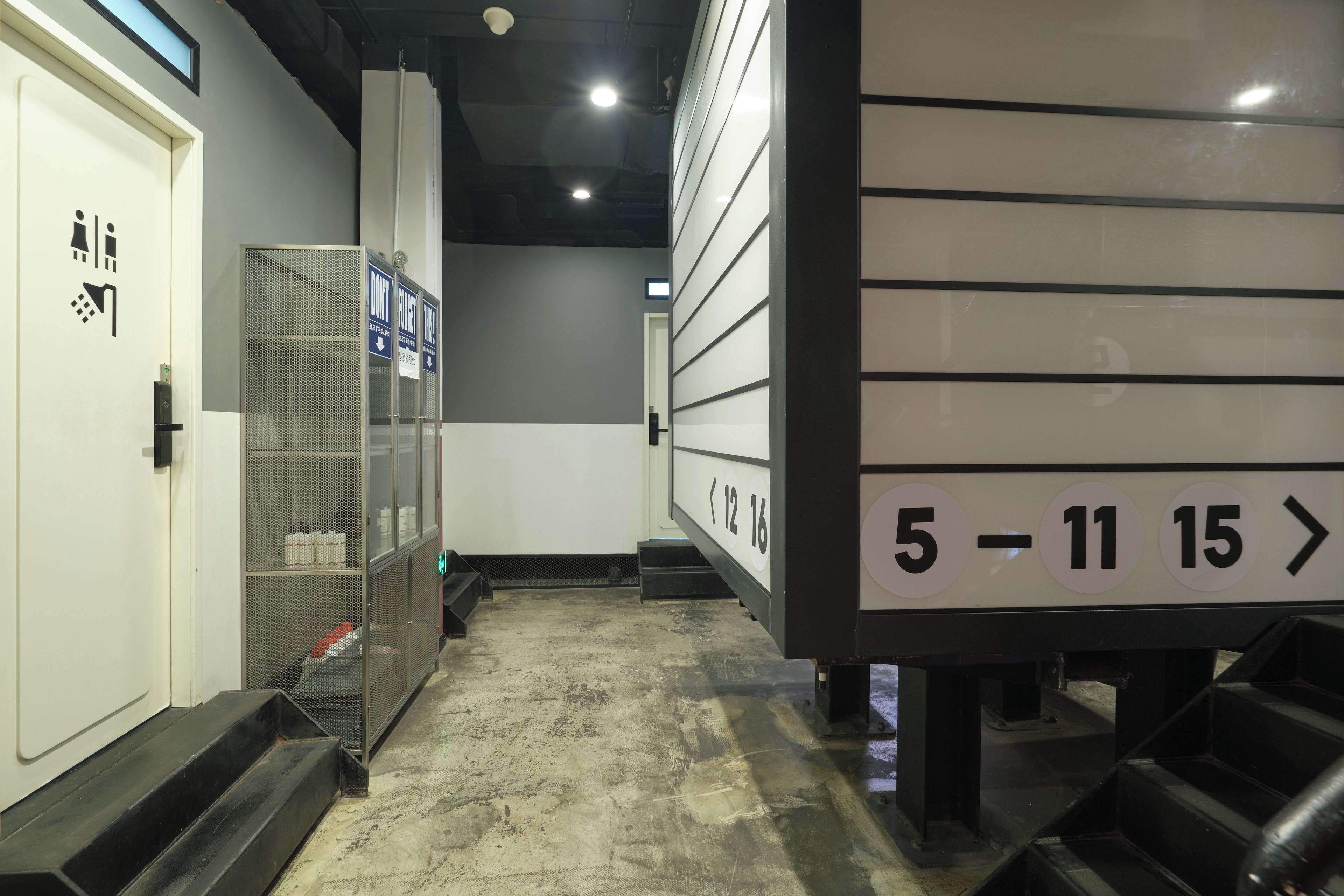 A hallway with a metal staircase, a door with a security lock, and directional signs with numbers.