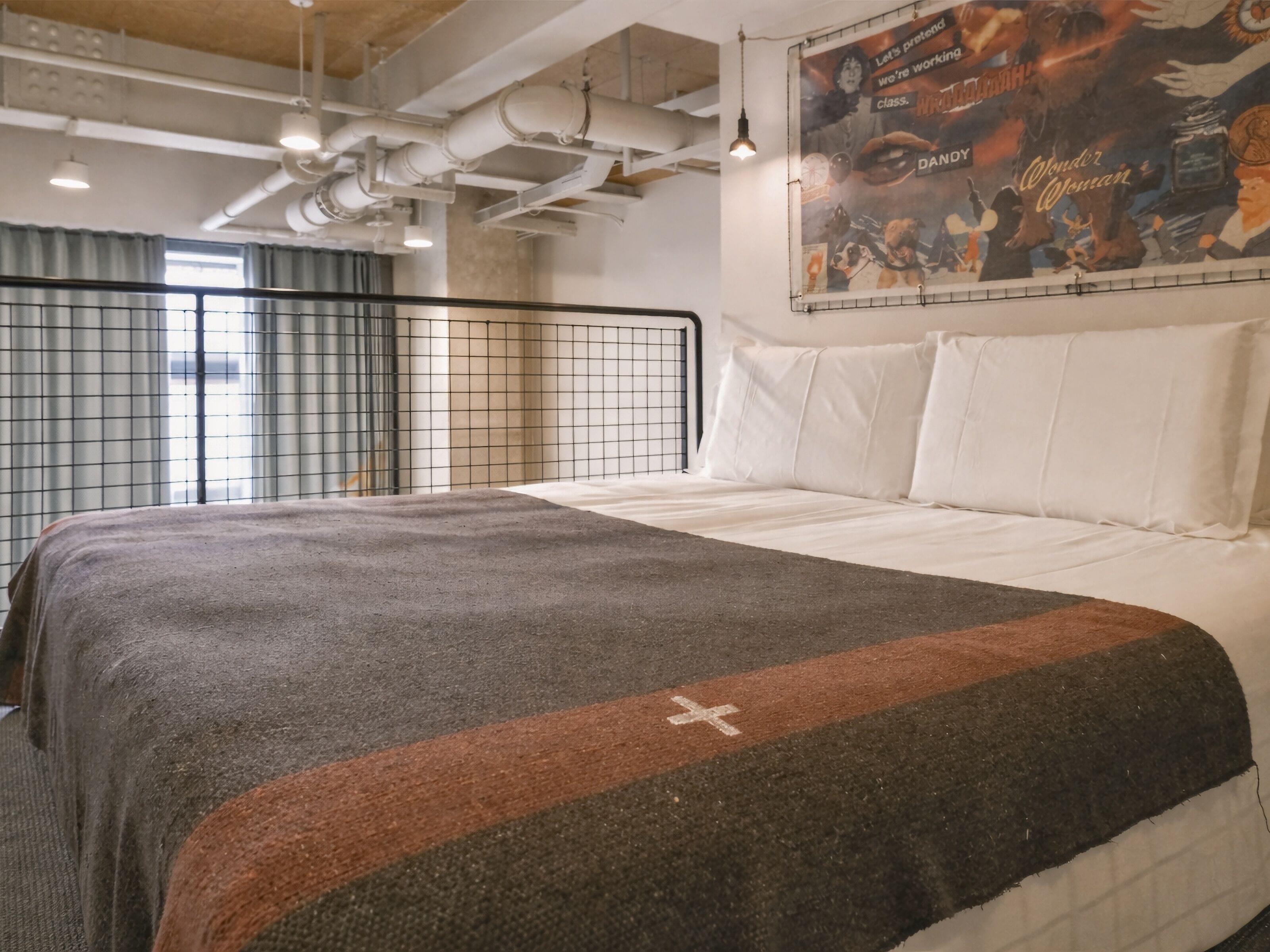 Een moderne hotelkamer met een groot bed, een grijze en bruine deken, een wit kussen, een metalen hoofdbord, en een poster aan de muur.