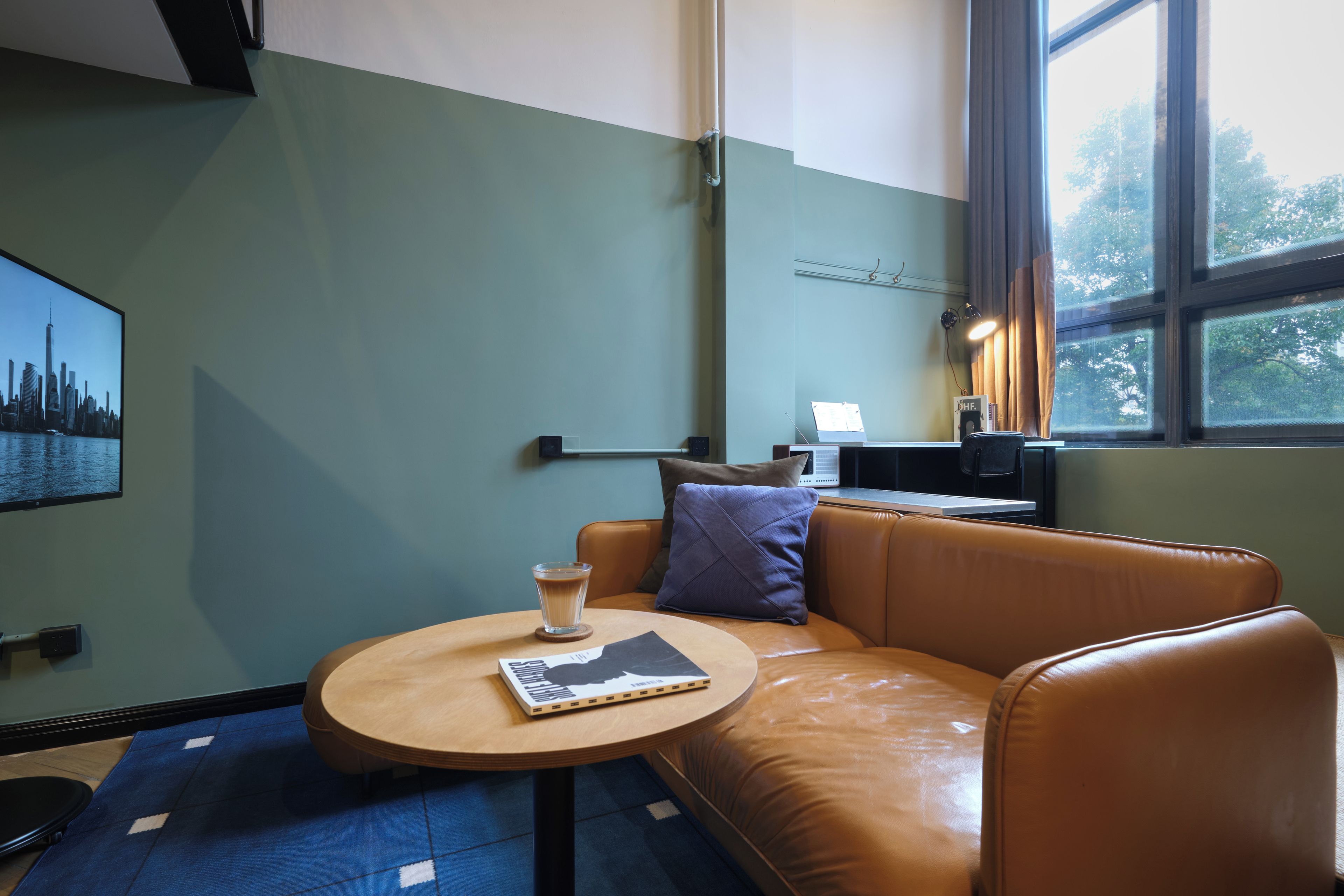 A modern interior with a leather sofa, a round table with a book and a glass of coffee, and a cityscape painting on the wall.