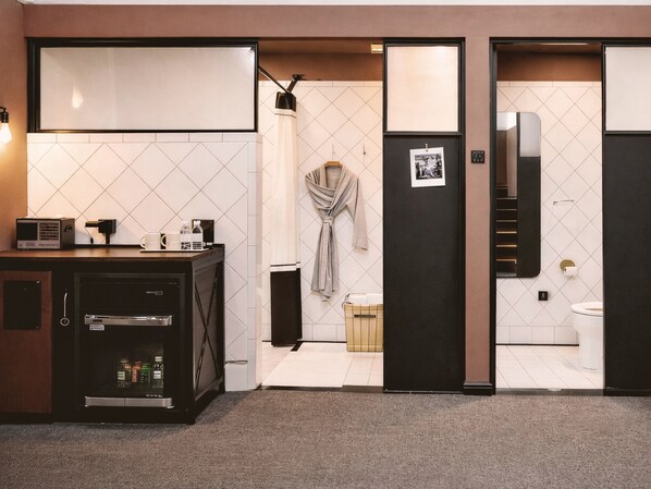 Une chambre d’hôtel avec une kitchenette, une salle de bain équipée de toilettes et d’une douche, et une robe accrochée au mur.