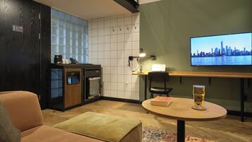 A modern living room with a sofa, a coffee table, a television displaying a cityscape, and a kitchenette area.