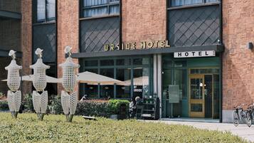 A hotel with a brick facade, a sign reading 'URSIDE HOTEL,' and outdoor seating with umbrellas.