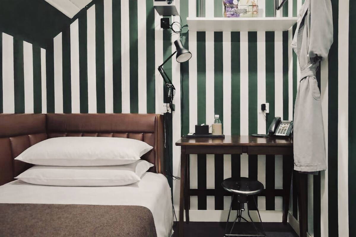 Een kleine, verzorgde kamer met een bed, nachtkastje en bureau met stoel.