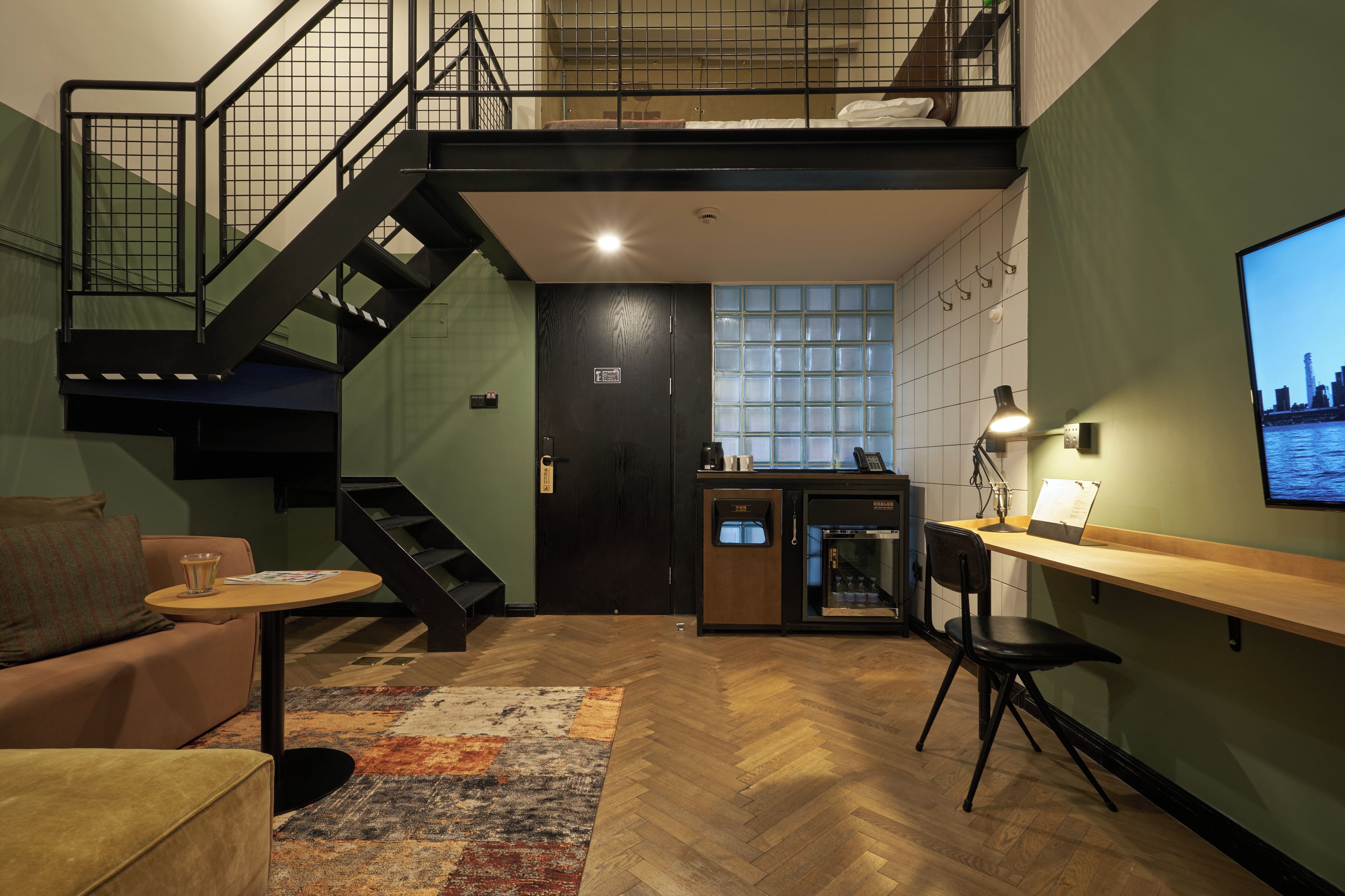 A modern loft-style room with a staircase, a kitchenette, a dining area, and a large window with a cityscape view.