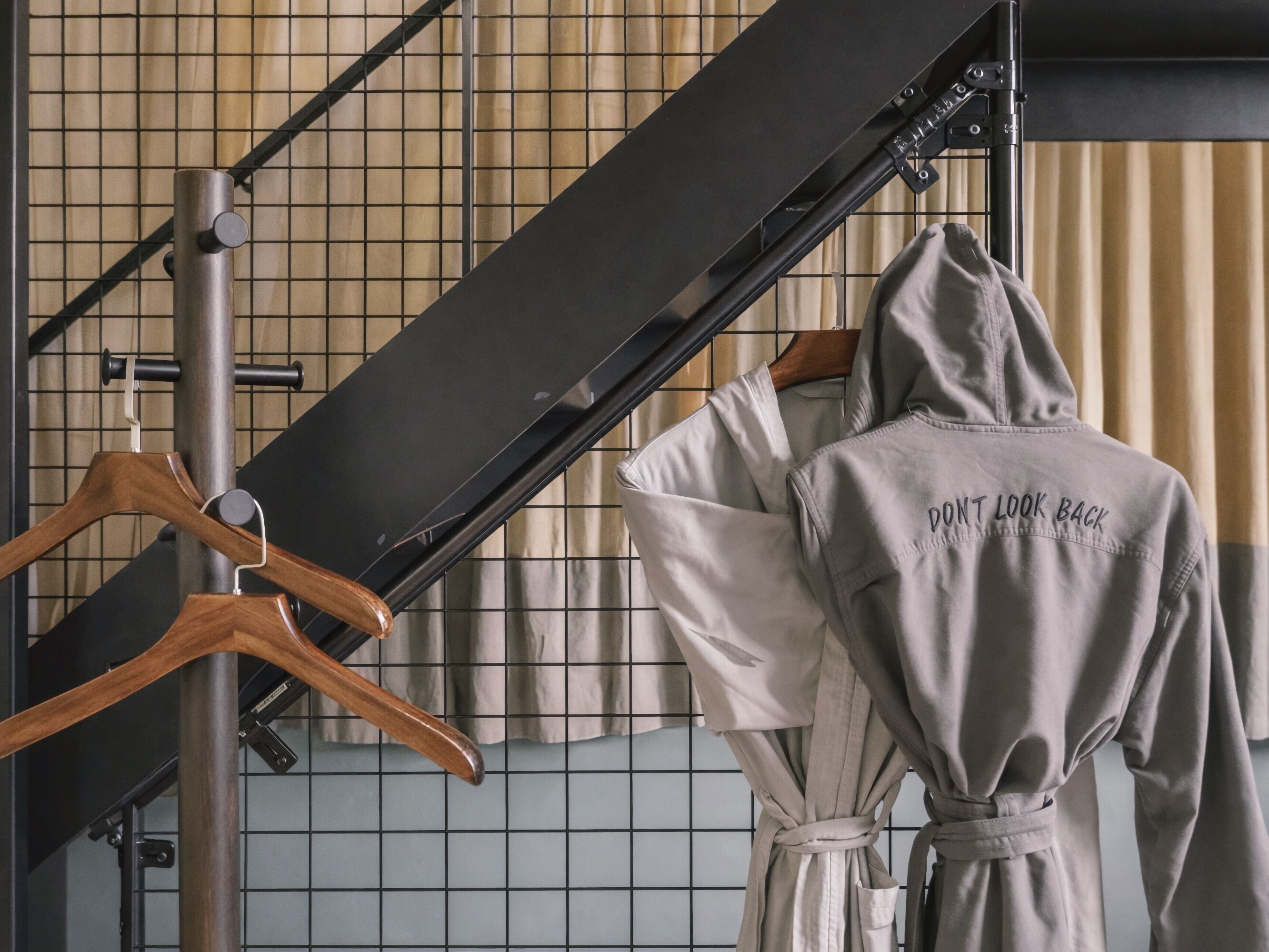 A hotel room with a metal staircase, a wooden hanger, and a robe with text on the back.