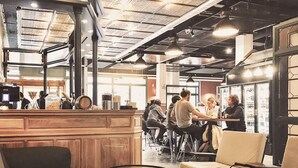 Un café avec des boiseries, des tables rondes et un plafond haut avec des poutres apparentes.